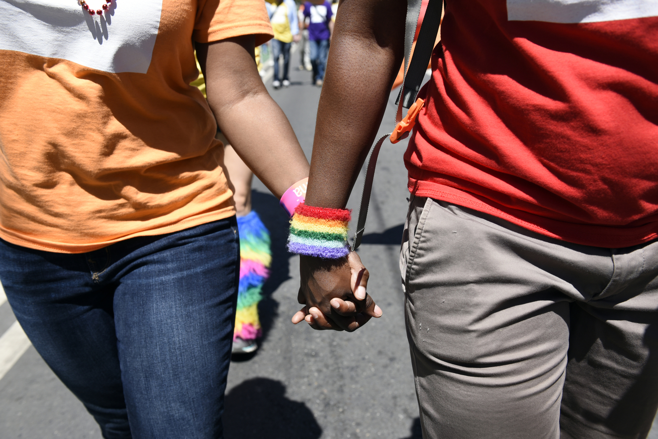 Image description: Two people holding hands, one wearing a rainbow sweatband on their wrist.